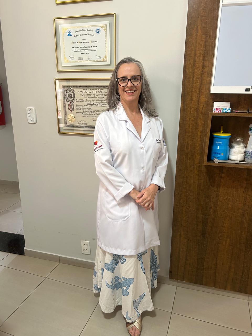 Dra. Thaisa Mattos em seu consultório, ao lado de seus diplomas
